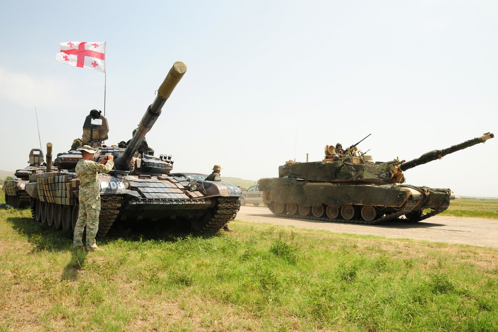 Georgian T-72 SIM-1 beside a U.S. M1A2 Abrams during Noble Partner 18 opening-ceremony practice. Vehicle / variant identification: Georgian T-72 SIM-1 and U.S. M1A2 Abrams. 30 July 2018. Vaziani Air Strip, Georgia. Strong comparative visual but not a combat photograph.