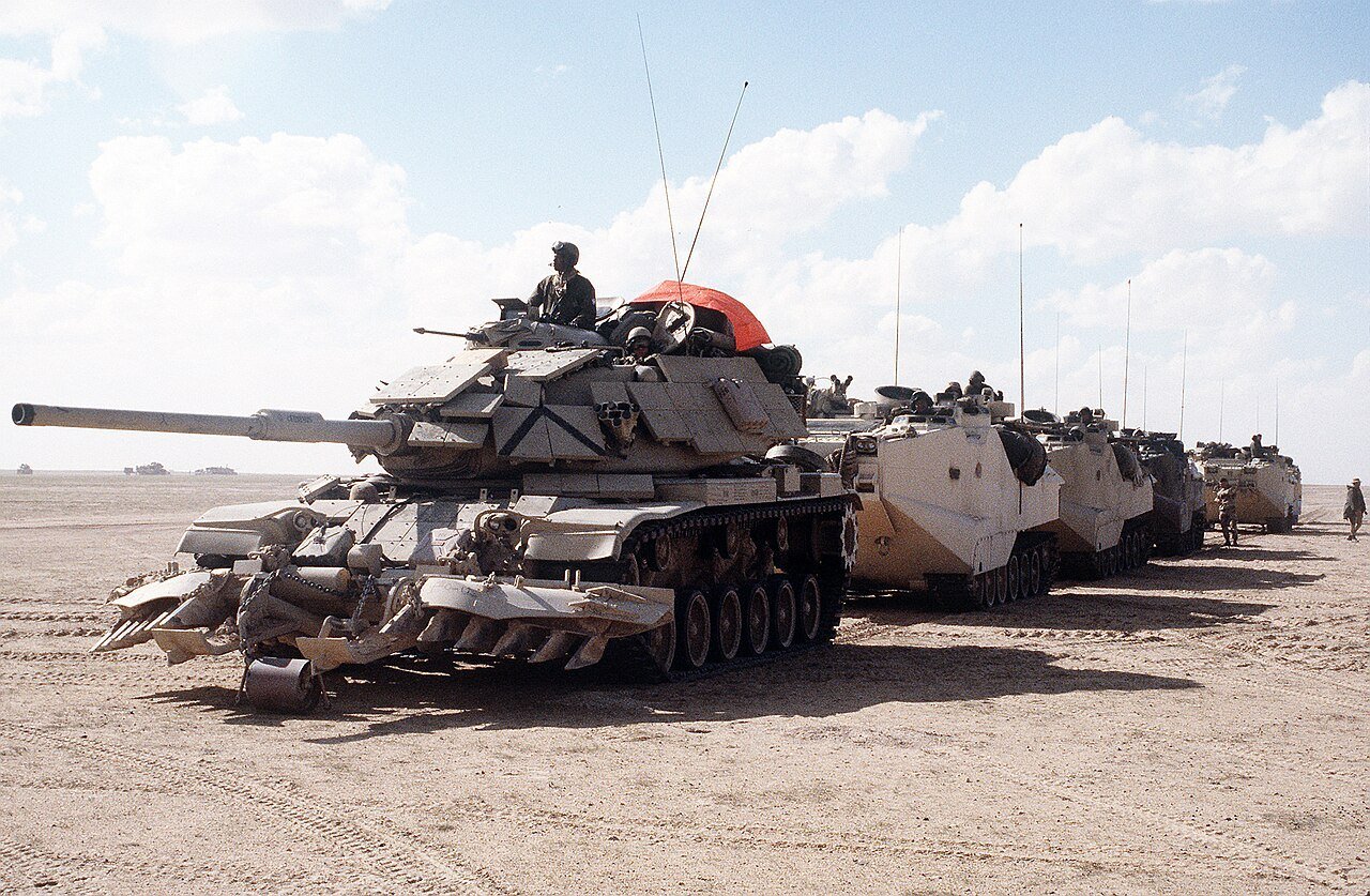 U.S. Marine Corps M60A1 with reactive armor and mine-clearing rollers/plows at the head of an AAVP-7A1 column as II MEF prepared to enter Kuwait at the start of the Desert Storm ground phase, 24 February 1991. Credit: Staff Sgt. Masters / U.S. military film record via Wikimedia Commons. Strong combat-service visual for late USMC M60A1 RISE Passive/ERA context.